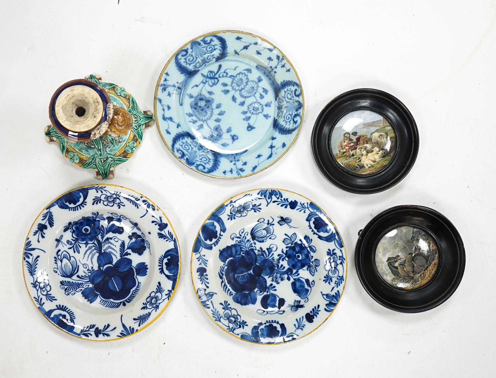 A group of 18th century delftware plates, Wedgwood majolica candlestand (a.f.) and two Victorian framed pot lids